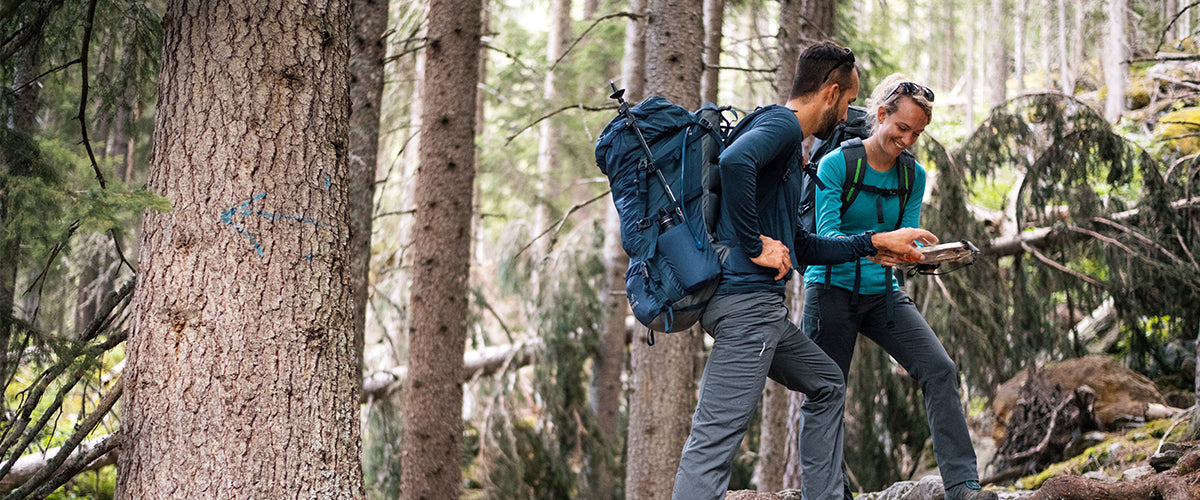 A man and woman hiking in the woods with backpacks on looking at their map