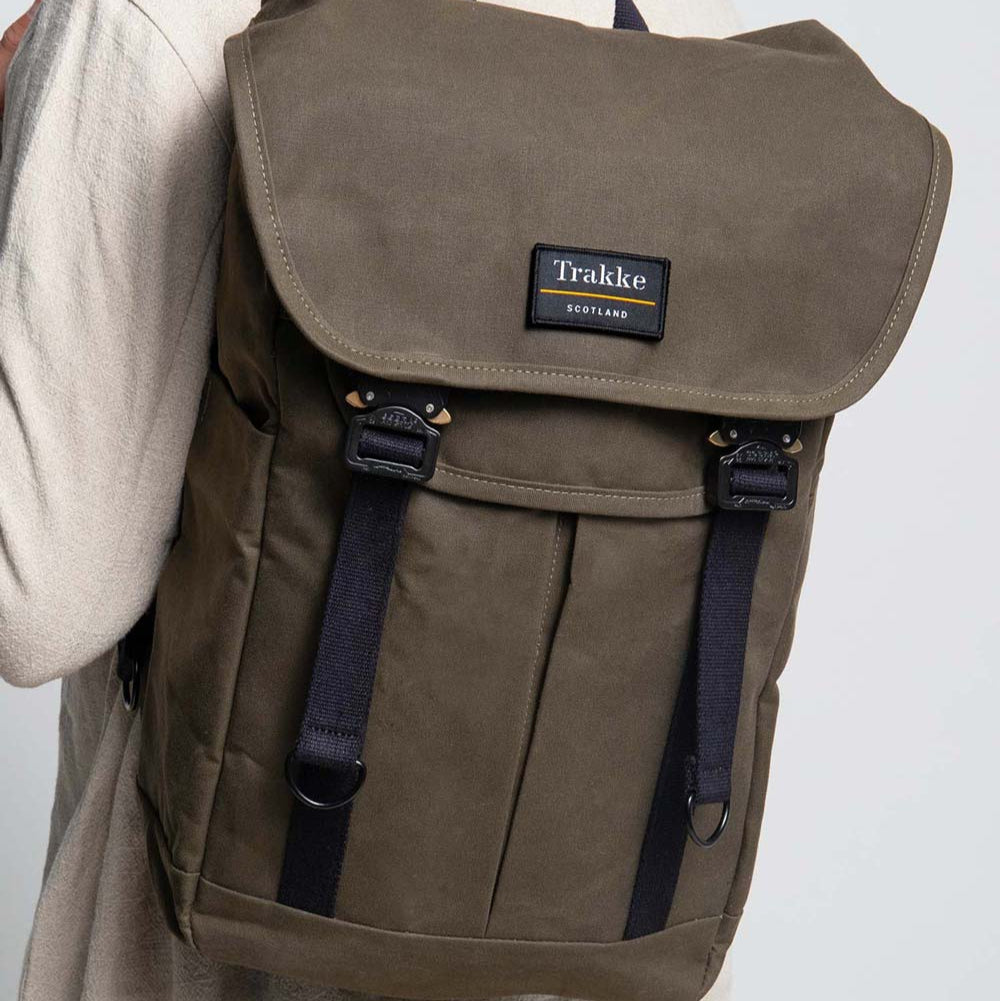 A male model is wearing the Trakke Bannoch Backpack in the Olive colourway. This version has the AustriAlpin COBRA clips on the backpack.