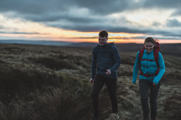 A man and a woman walking across moorland wearing wind resistant fleeces - action|bf