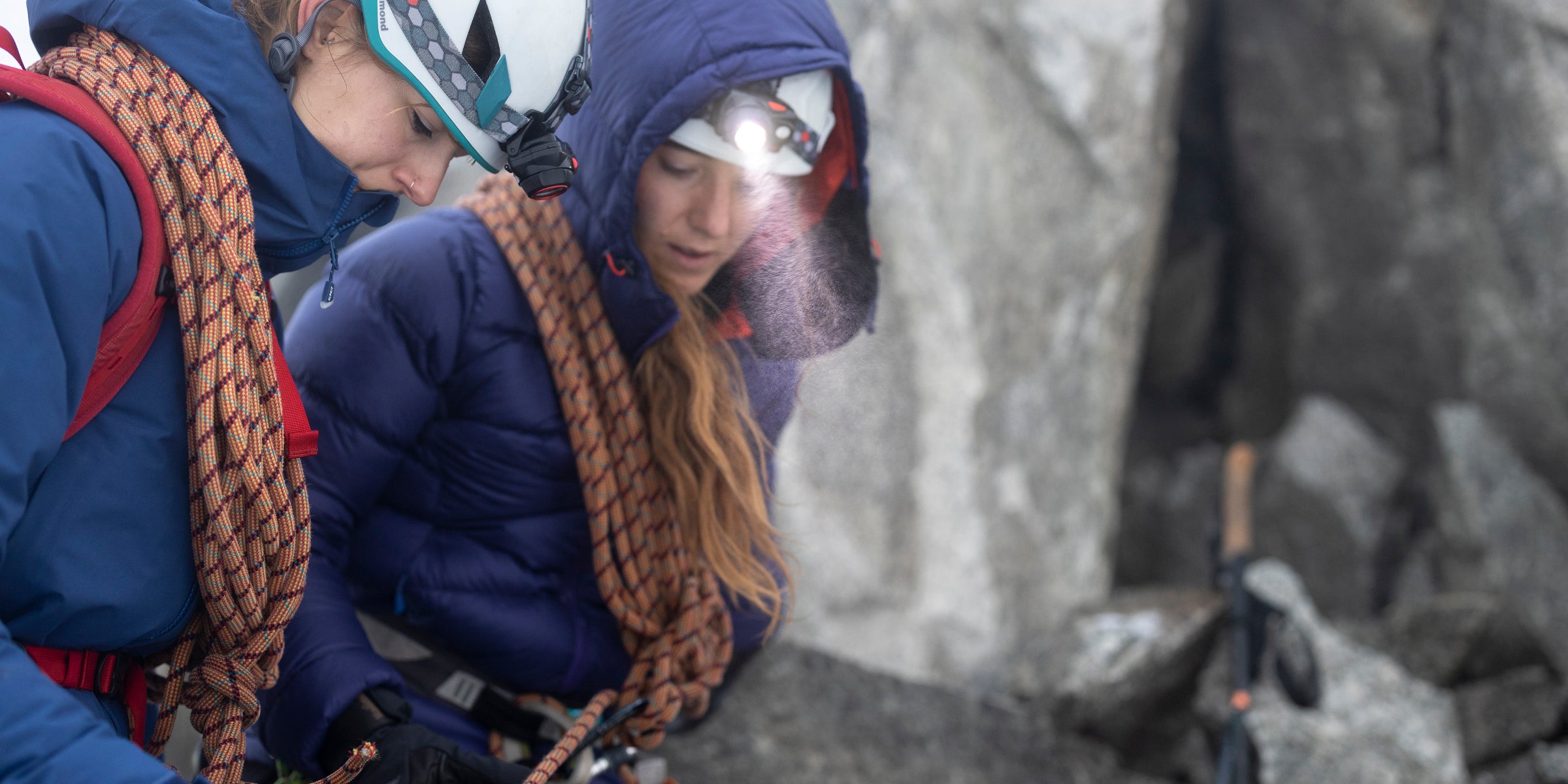 Two winter climbers wearing head torches on a belay