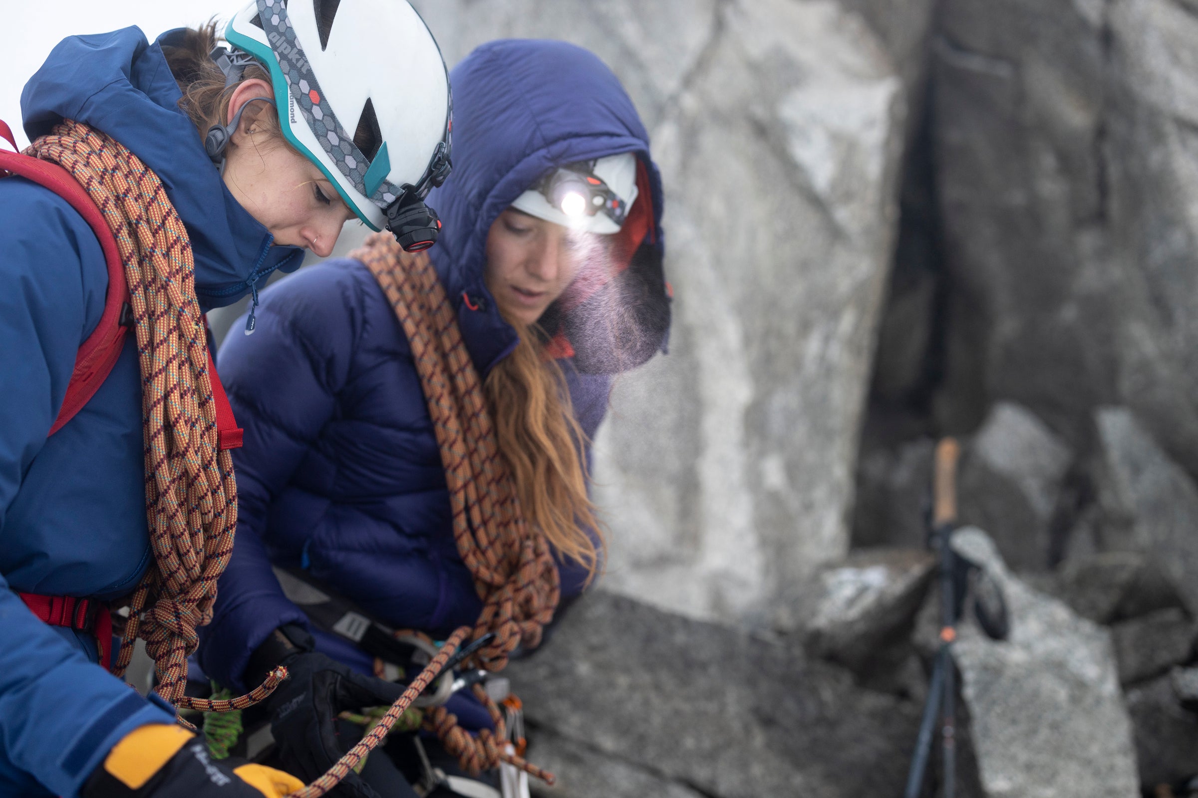 Two winter climbers wearing head torches on a belay