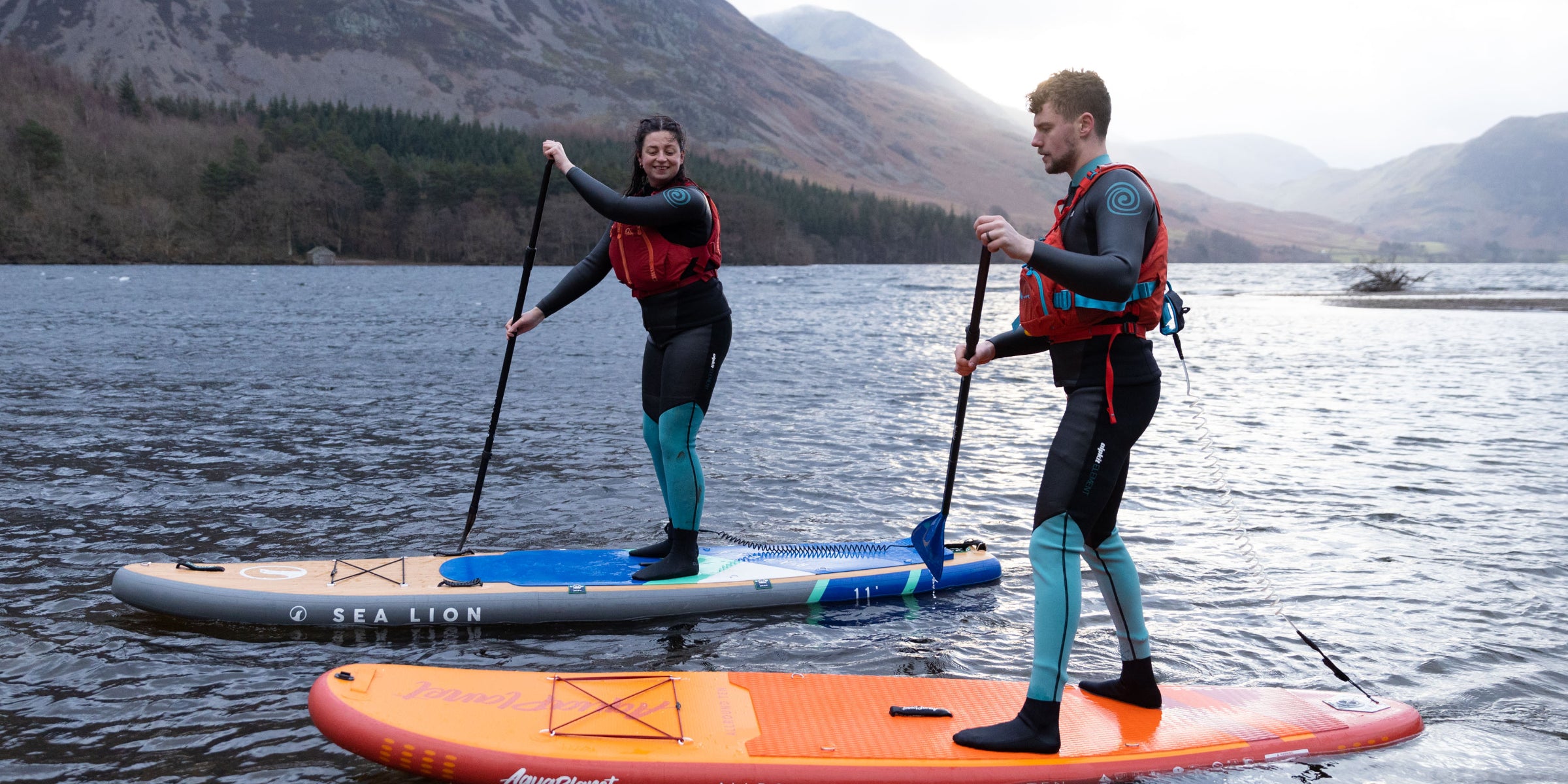 Paddle boarders in wetsuits paddle boarding in the Lake District