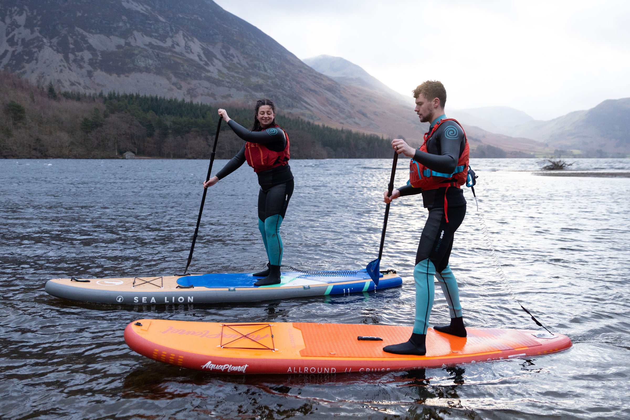 Paddle boarders in wetsuits paddle boarding in the Lake District