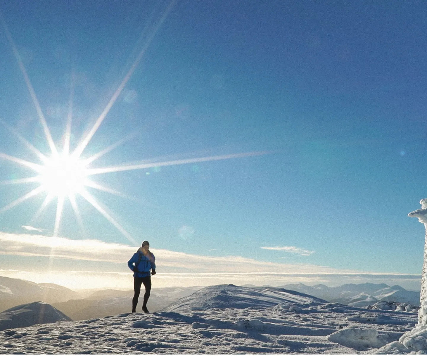 Runner running on a snowy mountain near a trig point