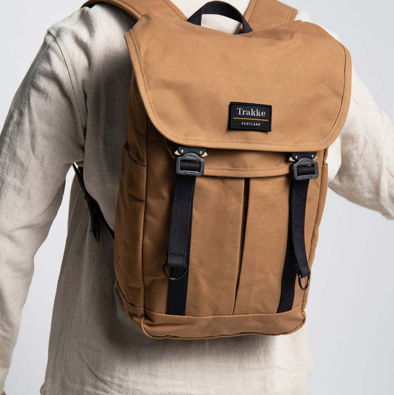 A man is wearing the Trakke Bannoch Backpack with COBRA Clips. The backpack is the Whisky colour. The Man is facing away from the camera with the focus on the backpack and he is swinging his arms