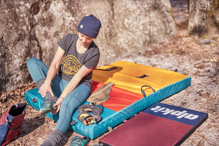 Zofia Reych taking their shoes off on the Origin taco bouldering mat - action - closed