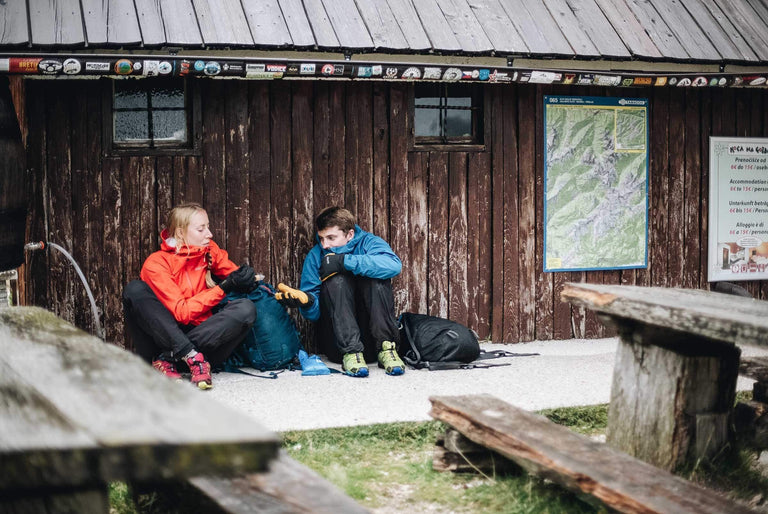 A man and a woman sat next to a wooden house in their waterproof clothing - action