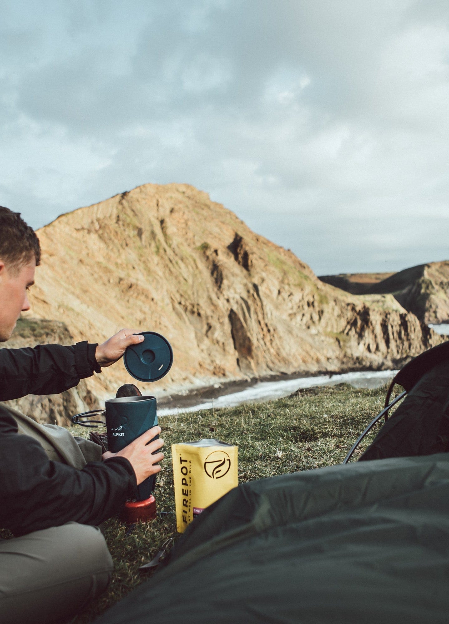 A man inspecting his stove sitting in front of his bivvy bag on the Devon coast - action - closed