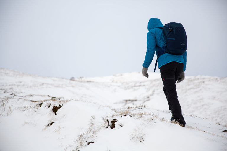 A man walking up a snowy bank on Kinder Scout in a blue insulated jacket - action - closed