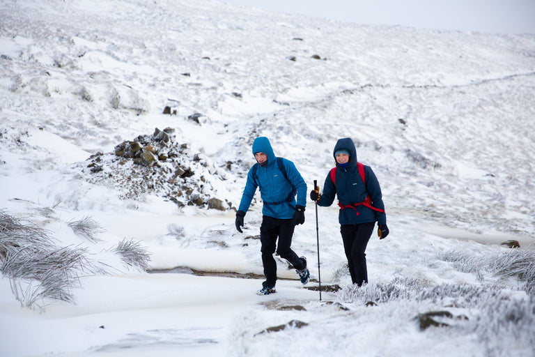 A man and a woman walking up a snowy bank on Kinder Scout in blue insulated jackets - action|sl