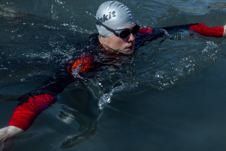 A man swimming in a coastal pool in an outdoor swimming wetsuit - action