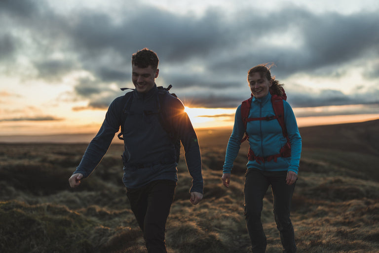 A man and a woman walking across moorland wearing wind resistant fleeces - action - closed