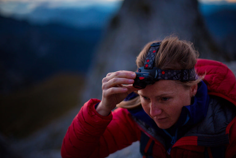 Woman using Alpkit Qark head torch in the mountains - action - closed