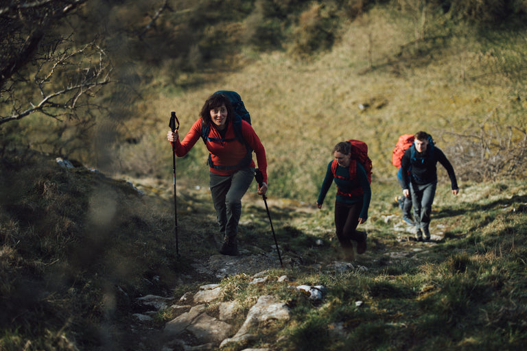 A group of people walking up a steep bank with trekking poles wearing fleeces and wool jumpers - action